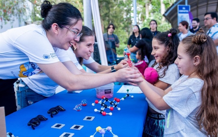 Imagen de unas niñas con unas estudiantes en los stands de los eventos.