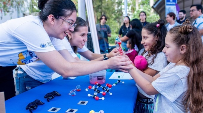 Imagen de unas niñas con unas estudiantes en los stands de los eventos.