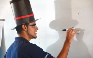 joven con sombrero de mago escribiendo en pizarra signos matemáticos