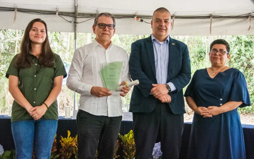 cuatro personas en un escenario, una de ellas recibe un reconocimiento