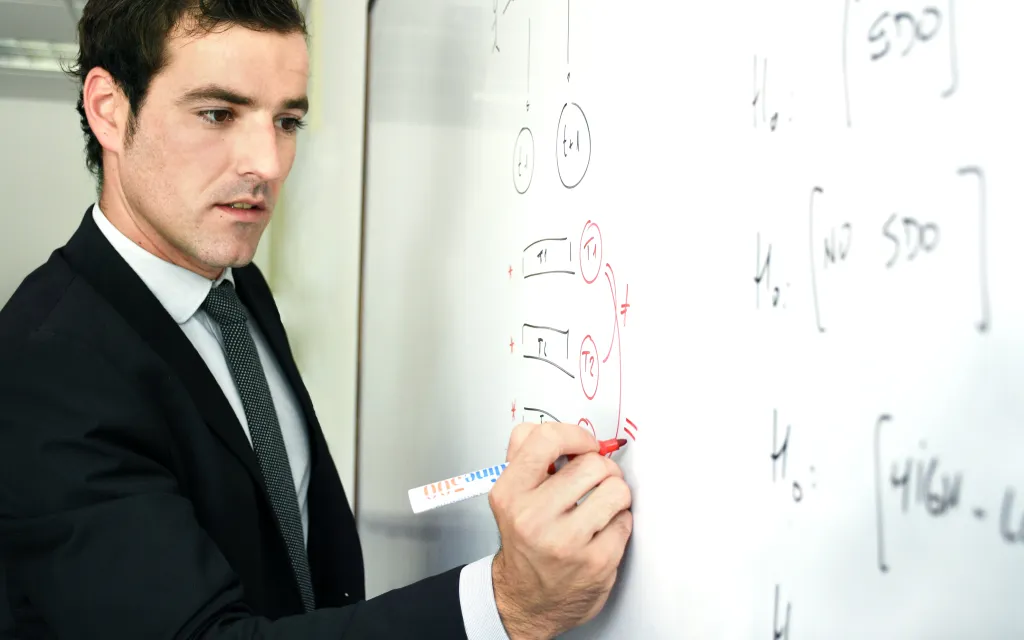Profesor escribiendo en pizarra. Persona docente escribiendo en pizarra.