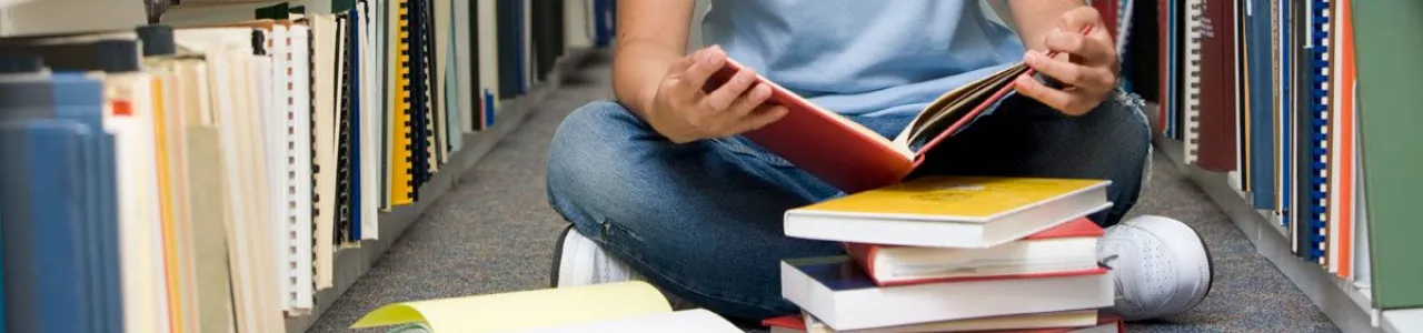 Estudiante sentado en el suelo leyendo libros