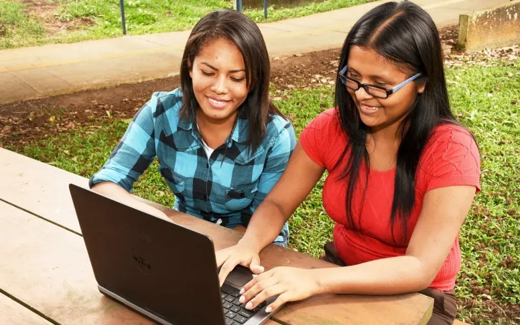 Estudiantes indígenas sentadas utilizando computadora.